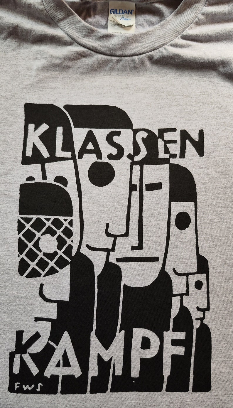May include: A gray t-shirt with a black graphic design. The graphic features a stylized image of three faces with the text "KLASSEN KAMPE" and "FWS" below.