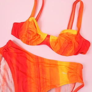May include: A two-piece swimsuit with a bright orange, yellow, and red ombre pattern. The top is a padded underwire bra with adjustable straps. The bottom is a high-waisted bikini bottom.