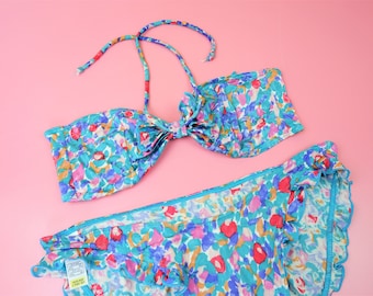 May include: A blue and white floral print bikini top and bottom. The top has a halter style with a bow in the front. The bottom has a ruffled edge.