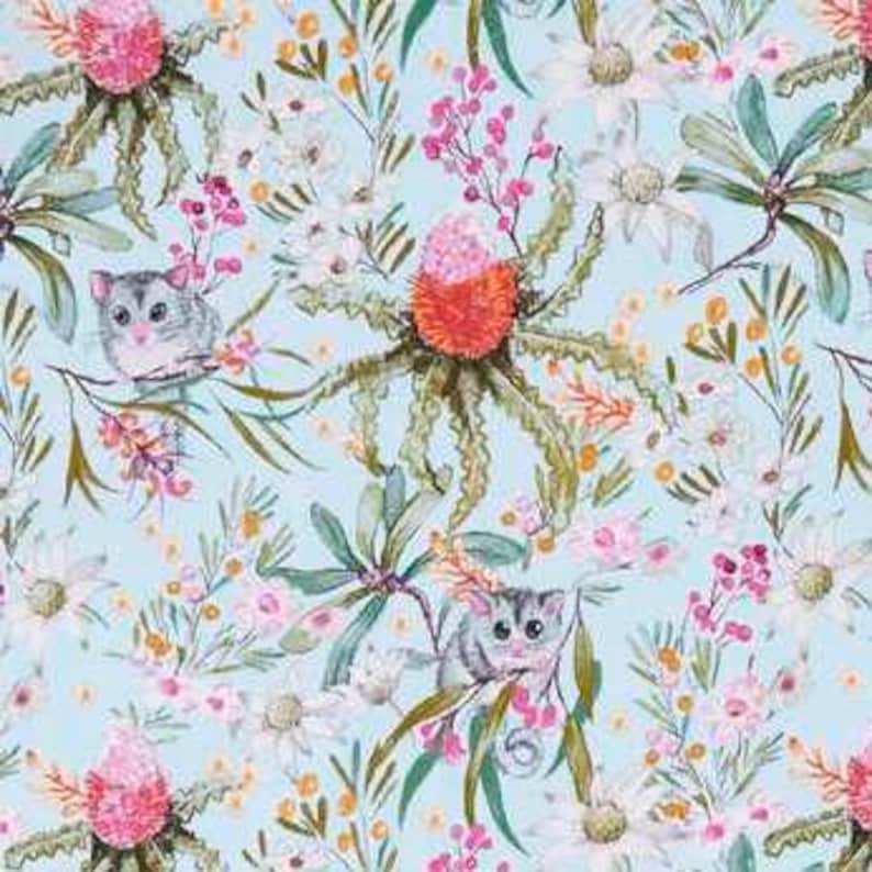 May include: A light blue fabric featuring a repeating watercolor pattern of grey possums, vibrant orange and pink banksia flowers, white wildflowers, and green foliage. The design showcases detailed botanical elements and small animals.