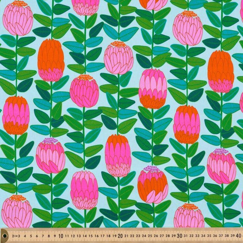 May include: A light blue fabric featuring a repeating pattern of vertical stems with green leaves and rounded flower heads in shades of pink and orange. A measuring tape is visible at the bottom, showing a scale from 0 to 40 inches.