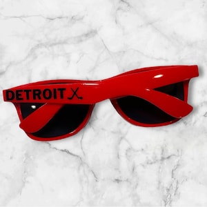 May include: Red sunglasses with black text that says "DETROIT X" on the left side of the frame.