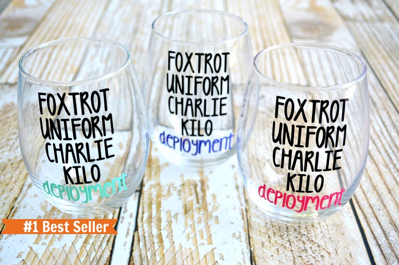 May include: Three clear glass wine glasses with black lettering that reads "FOXTROT UNIFORM CHARLIE KILO deployment". The glasses are on a light brown wooden surface. #1 Best Seller