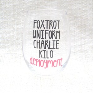 May include: A clear glass wine glass with the text "FOXTROT UNIFORM CHARLIE KILO DEPLOYMENT" printed on it. The word "DEPLOYMENT" is in pink lettering.