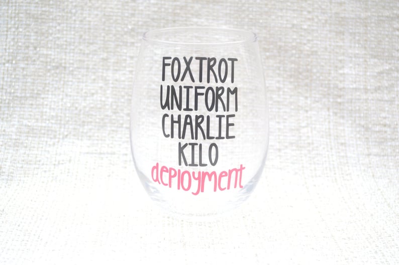 May include: A clear glass wine glass with the text "FOXTROT UNIFORM CHARLIE KILO DEPLOYMENT" printed on it. The word "DEPLOYMENT" is in pink lettering.