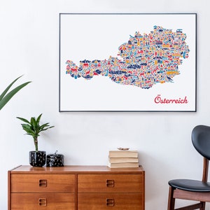 May include: A colorful illustration of Austria, with the word "&Ouml;sterreich" in red at the bottom. The map is made up of small icons representing different aspects of Austrian culture, such as buildings, mountains, and animals. The illustration is framed and hanging on a white wall above a wooden dresser.