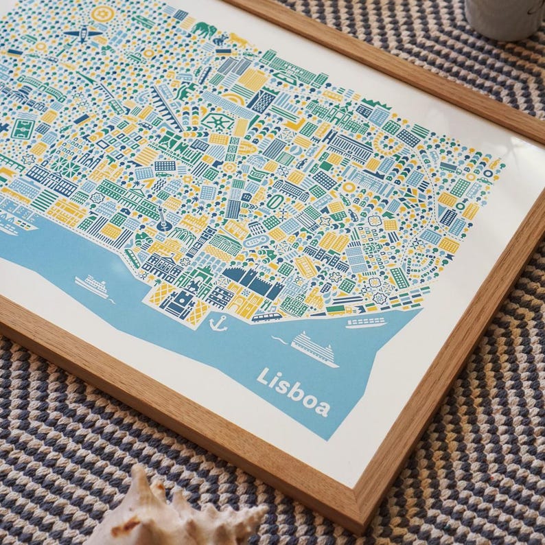 May include: A framed art print of Lisbon, Portugal, featuring a detailed, colorful map illustration. The map uses blue, yellow, and green hues to depict the city's layout, with the word "Lisboa" printed in white. The print is set in a natural wood frame.
