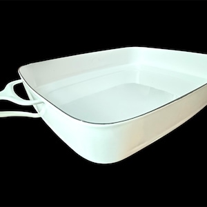 May include: A white, triangular baking dish with a handle on one side. The dish has a thin, dark gray trim around the rim. The handle is a continuation of the dish's design, with a curved shape for easy gripping. The dish is empty and sits against a black background.