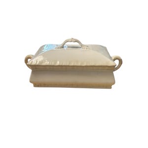 May include: Cream-colored, square ceramic serving dish with a lid. The dish has a decorative handle on the lid and curved handles on the sides. The dish is elevated on a base.