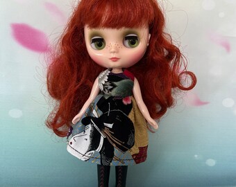 May include: A doll with red hair and green eyes wearing a patterned dress with black boots. The dress features a design with a geisha and floral elements. The doll has a fair complexion and is posed against a soft background.