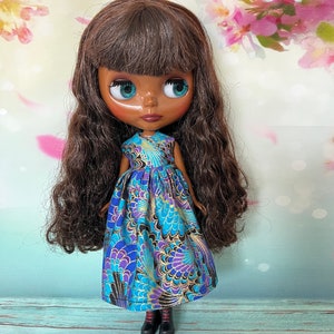 May include: A doll with brown hair and teal eyes wearing a blue dress with a gold and purple floral pattern. The doll is wearing black boots with red laces. The background is a floral design.