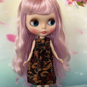 May include: A doll with long, lavender hair and large blue eyes. The doll wears a black dress with a repeating skull and rose pattern. The dress has the words "Old School" printed on it.