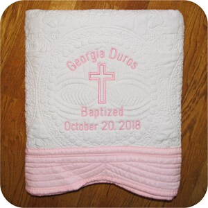 Pode incluir: Cobertor de beb&ecirc; acolchoado branco com borda rosa. O cobertor &eacute; bordado com o nome "Georgia Duros", uma cruz e o texto "Batizada em 20 de outubro de 2018".