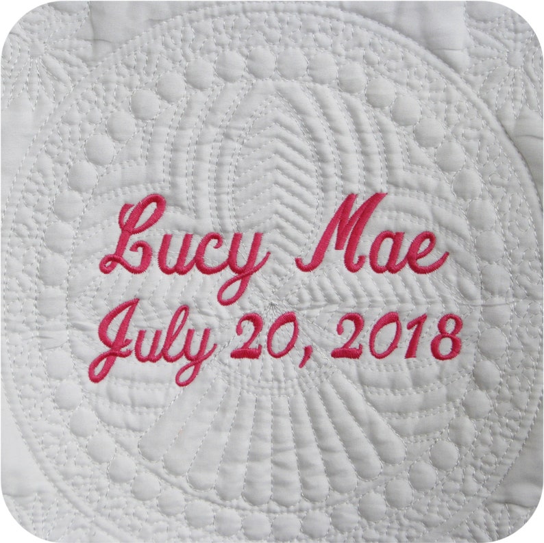 Pode incluir: Tecido acolchoado branco com texto bordado em rosa que diz "Lucy Mae July 20, 2018".