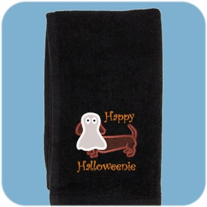 May include: Black towel with an embroidered image of a dachshund wearing a ghost costume. The text "Happy Halloweenie" is embroidered below the dog.