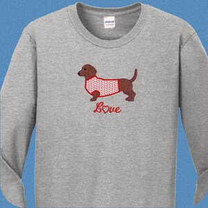 May include: A gray long-sleeved t-shirt with a red embroidered dachshund wearing a red and white heart patterned shirt. The text "Love" is embroidered below the dachshund with a red heart.