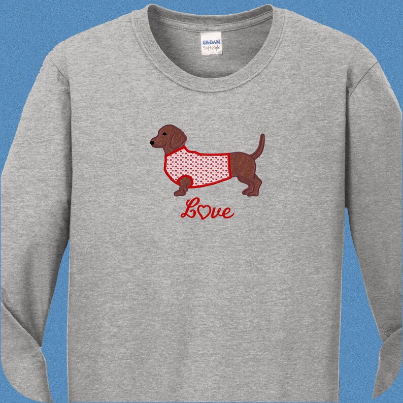May include: A gray long-sleeved t-shirt with a red embroidered dachshund wearing a red and white heart patterned shirt. The text "Love" is embroidered below the dachshund with a red heart.