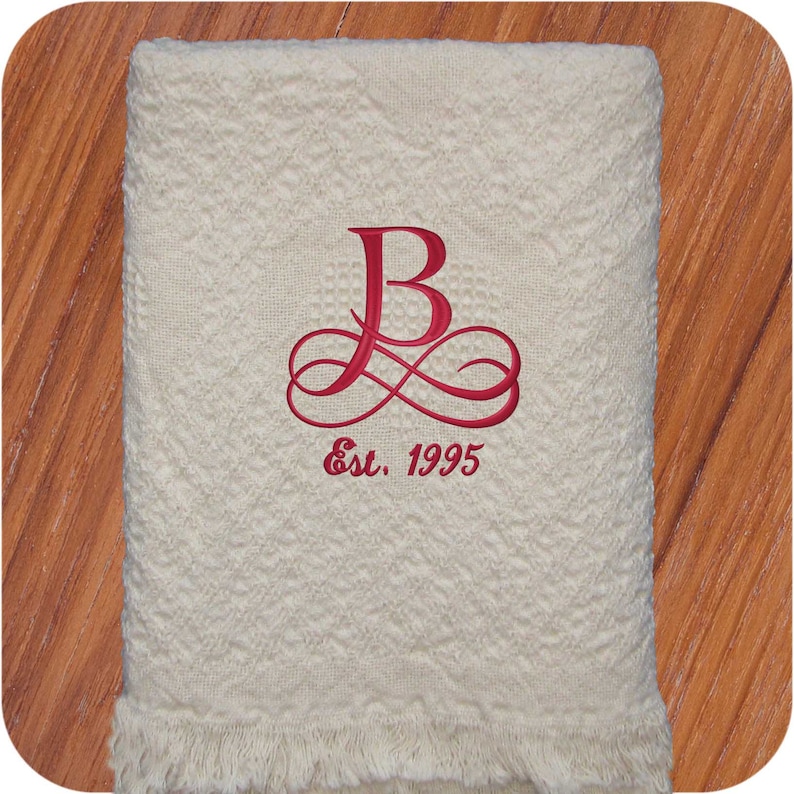 Natural colored cotton heart weave patterned throw blanket with fringe.  A personalized embroidery design on the blanket is a large red B with double infinity swirls below.  'Est. 1995' below in read thread.  The custom monogram is on the bottom center and makes a delightful and elegant anniversary or wedding gift.