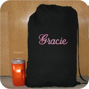 A black canvas or cotton drawstring bag with shoulder strap and the name 'Gracie' embroidered in pink thread in the Diane Script font.