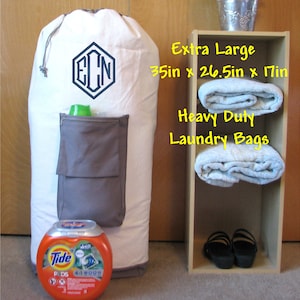 An extra large, heavy duty white laundry bag with gray trim and gray zippered pocket containing laundry detergent is in front of a closet. The laundry bag is monogrammed with 3 letter initials "ECN" surrounded by a hexagon frame embroidered in navy thread with the 3 Letter Point design.