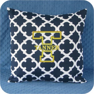 May include: A navy blue and white patterned throw pillow with a gold embroidered letter "T" and the name "TANNER" underneath.