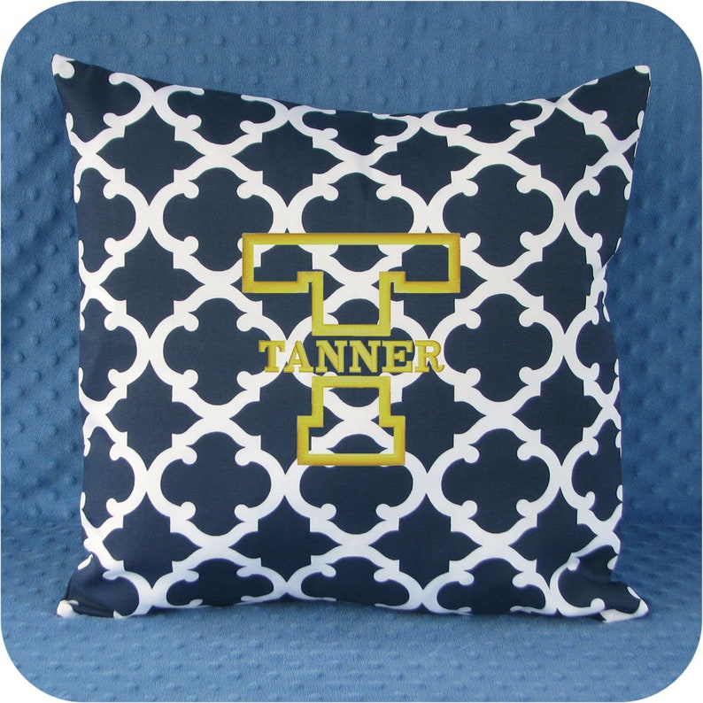 May include: A navy blue and white patterned throw pillow with a gold embroidered letter "T" and the name "TANNER" underneath.