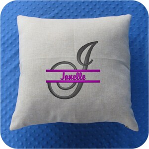 Puede incluir: Una almohada beige con una letra J bordada en gris y el nombre "Janelle" en letras moradas.