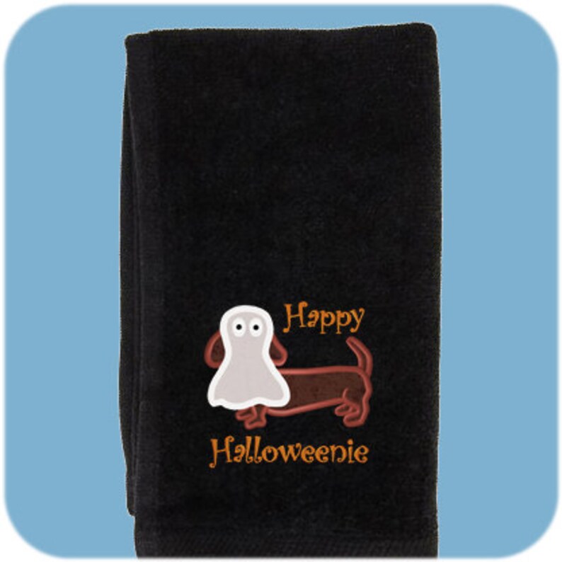 May include: Black kitchen towel with an embroidered image of a dachshund wearing a ghost costume. The text "Happy Halloweenie" is embroidered below the dog.