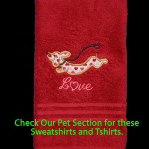 May include: A red hand towel featuring an embroidered dachshund dog with a white body covered in red and pink hearts, a black leash, and the word Love in pink script. The text Check Our Pet Section for these Sweatshirts and Tshirts is visible.