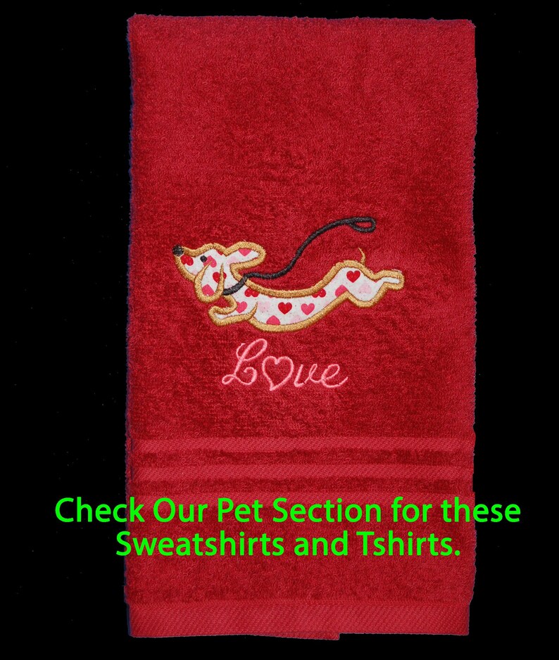 May include: A red hand towel featuring an embroidered dachshund dog with a white body covered in red and pink hearts, a black leash, and the word Love in pink script. The text Check Our Pet Section for these Sweatshirts and Tshirts is visible.