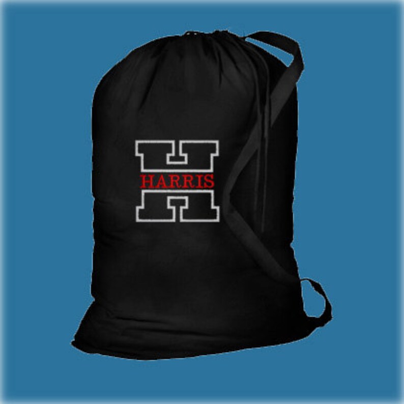 A black drawstring cotton or canvas laundry bag with a white outlined capital H and the word 'HARRIS' in red thread inside the letter.