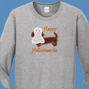 May include: A grey long-sleeved t-shirt with a brown dachshund wearing a white ghost costume. The text "Happy Halloweenie" is printed on the shirt.