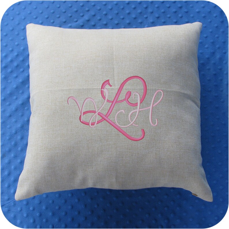 Puede incluir: Una almohada de lino beige con un monograma bordado en rosa de las letras "LH" en una fuente cursiva.