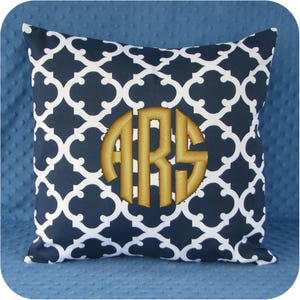 Puede incluir: Una almohada de color azul marino y blanco con un monograma dorado "ARS" bordado en el centro.