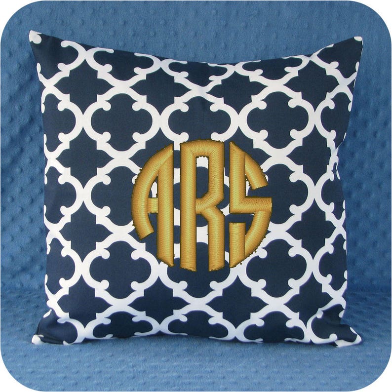 Puede incluir: Una almohada de color azul marino y blanco con un monograma dorado "ARS" bordado en el centro.