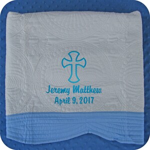 Pode incluir: Cobertor de beb&ecirc; acolchoado branco com borda azul. O cobertor tem uma cruz bordada em azul e o texto "Jeremy Matthew April 9, 2017".