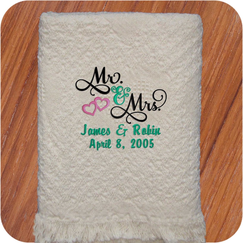 Natural colored cotton heart weave patterned throw blanket with fringe. Embroidery design on the blanket is Mr. & Mrs. in black thread, 2 entwined pink hearts and couples' first names and wedding or anniversary date below in teal thread using the Mr & Mrs design.  The perfect wedding gift!