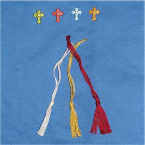 May include: Four decorative cross charms in yellow, red, light blue, and gold are displayed above four braided tassels in white, gold, and red. The tassels are arranged on a blue background, creating a visually appealing arrangement.