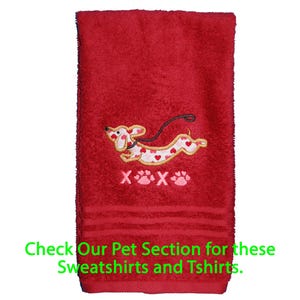 May include: A red hand towel featuring an embroidered dachshund dog with a white body covered in small red and pink hearts. Below the dog, the text reads X paw print X paw print. The green text at the bottom says Check Our Pet Section for these Sweatshirts and Tshirts.
