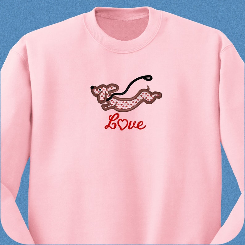 May include: Pink sweatshirt with a red dachshund with a heart pattern running with a leash. The text "Love" is below the dachshund.