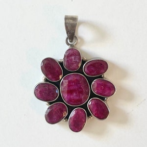 May include: A silver pendant featuring a cluster of eight ruby-coloured gemstones arranged in a flower design.