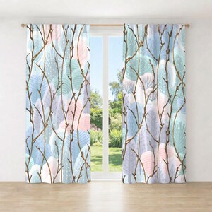 a pair of curtains with a pattern of branches and leaves in various shades of blue, pink, and green. The curtains are hanging from a rod, and there is a view of a garden through the window behind them.