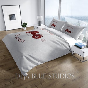 May include: A light gray bed set featuring a red tractor graphic and the text "Jackson Farms" and "1930". The set includes a duvet cover and two pillowcases. The bedding is on a bed in a well-lit room.