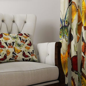 May include: A white armchair with a tufted back and a pillow featuring a colorful butterfly pattern. The armchair is in front of a curtain with a similar butterfly pattern.