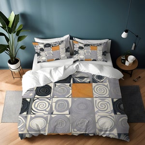 May include: A duvet cover with a geometric pattern of gray, white, and orange squares and circles. The duvet cover is on a bed with white pillows and a white comforter.