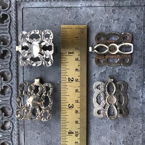 May include: Four silver-toned metal buckles with intricate designs. The buckles are approximately 1 inch in size and have a slightly aged appearance.