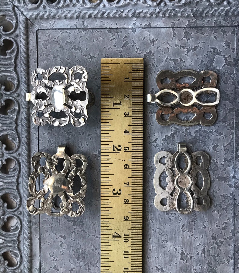 May include: Four silver-toned metal buckles with intricate designs. The buckles are approximately 1 inch in size and have a slightly aged appearance.