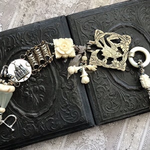 May include: A white and silver charm bracelet with a variety of charms, including a small house, a flower, and a bird. The bracelet is on a black background.