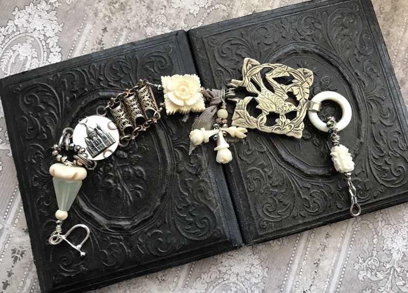 May include: A white and silver charm bracelet with a variety of charms, including a small house, a flower, and a bird. The bracelet is on a black background.
