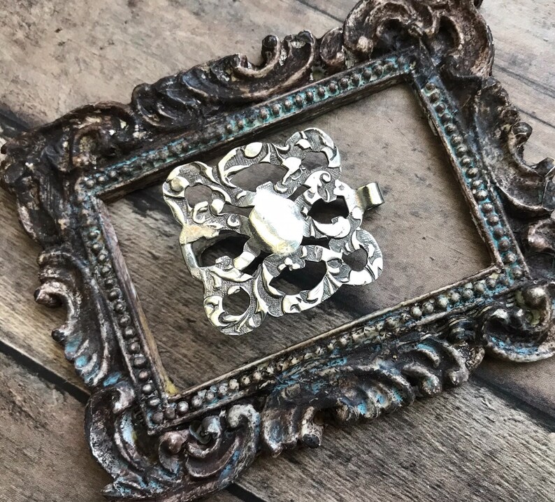 May include: A silver filigree buckle with a decorative design. The buckle is in a vintage style and has a delicate, intricate pattern.